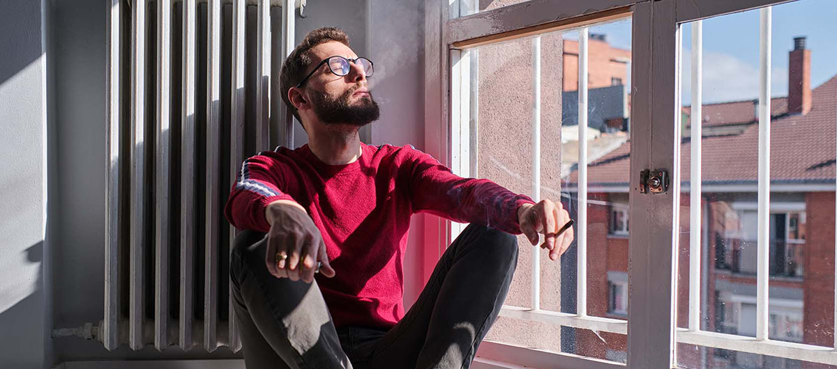 Man in Ajax Ontario smoking BC God Bud Strain weed in a joint sitting in a window at home. Buy weed near me. Cannabis dispensary in Ajax, Whitby, and Pickering.